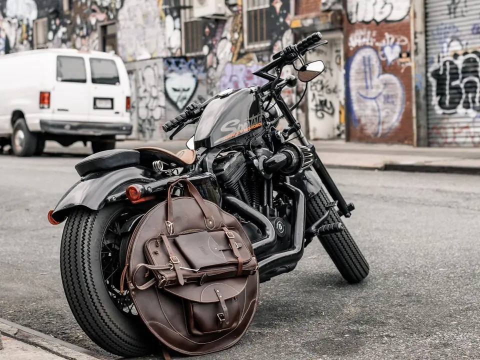 A leather cymbal backpack strapped to a motorbike on a graffiti-lined street