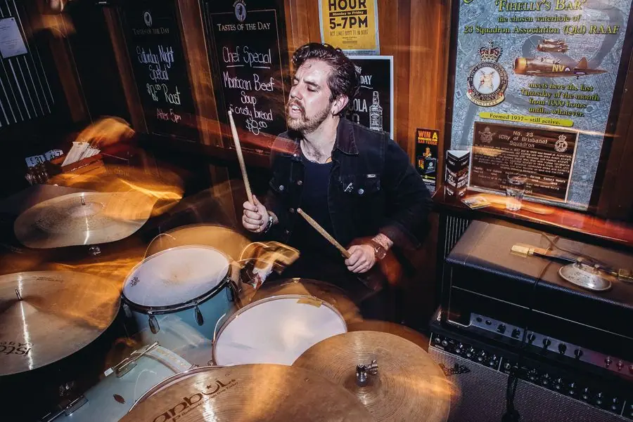 Jared playing a kit in a pub, sticks blurred mid-stroke